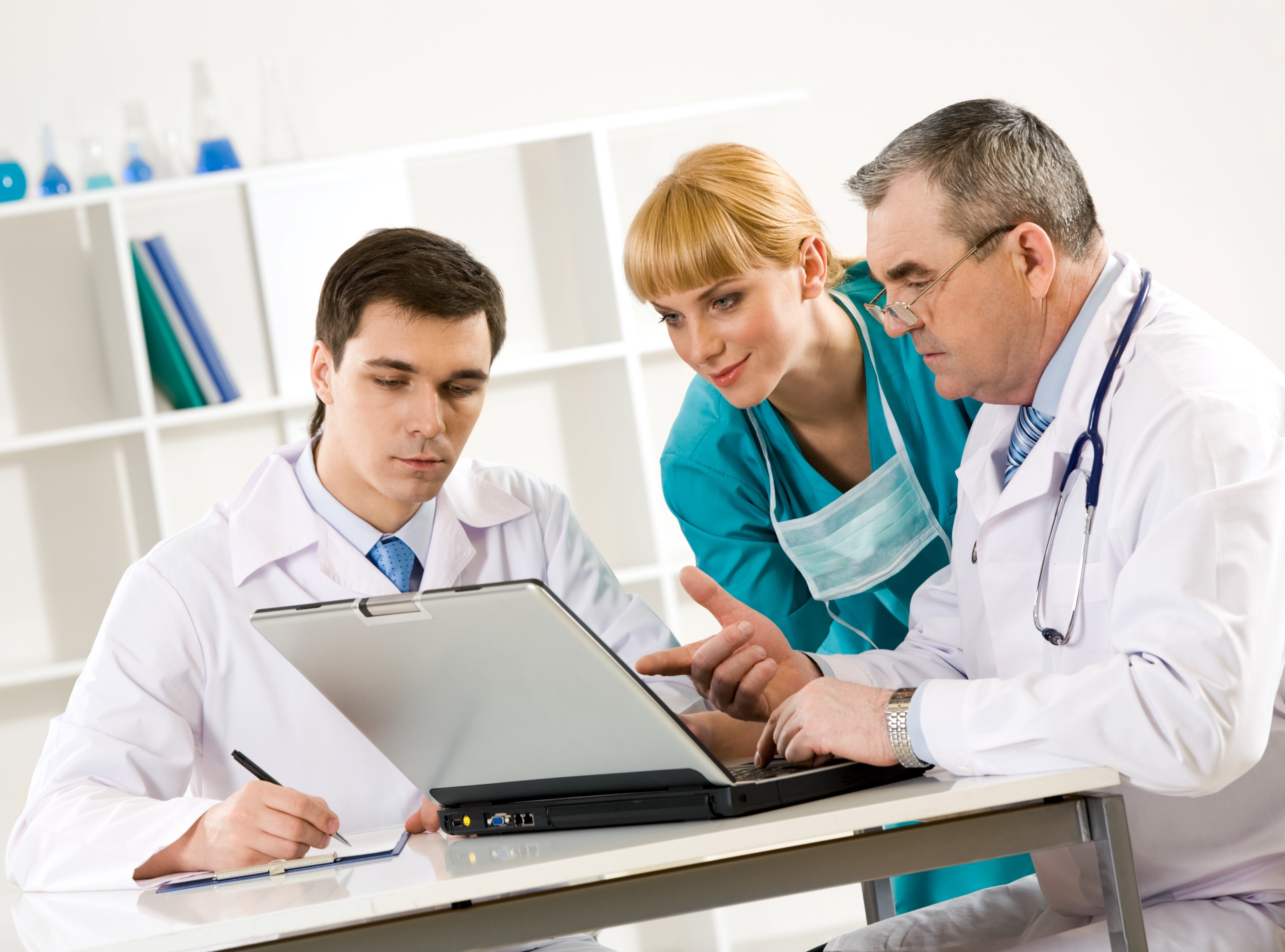 photo-of-aged-physician-pointing-at-laptop-display-with-two-colleagues-near-by-looking-SBI-300908685